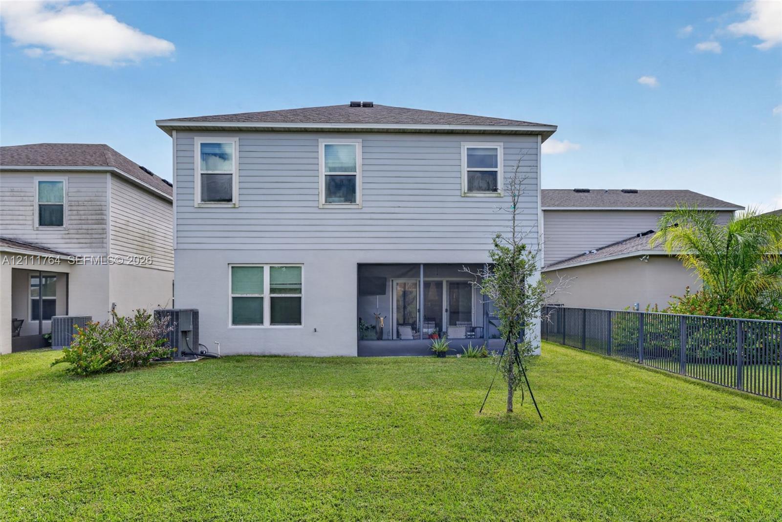 Two-story exterior featuring light-toned horizontal siding, a screened-in lanai, and an expansive grass lawn enclosed by metal fencing