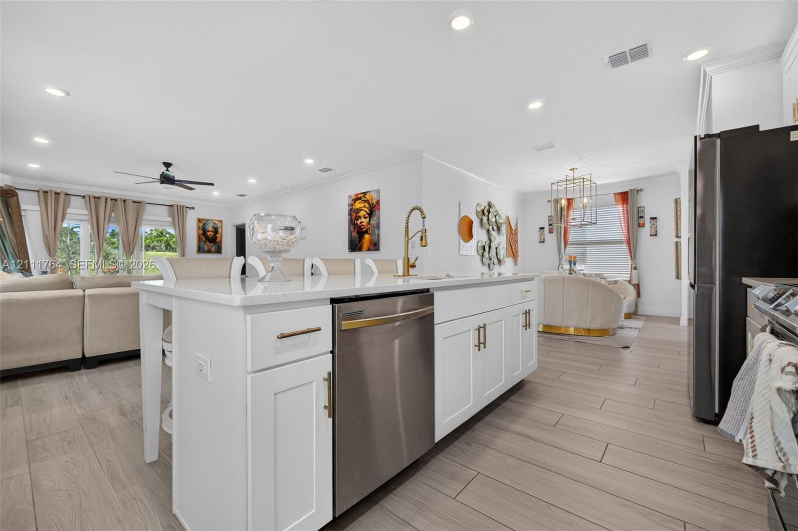 Kitchen featuring a large central island with white shaker cabinetry, quartz countertops, a brass pull-down faucet, and recessed ceiling lighting throughout, complemented by wood-finish floor tiling