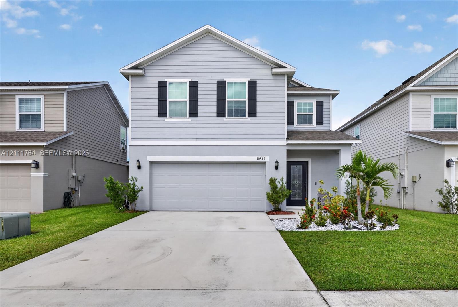 Two-story residence featuring light gray horizontal siding, dark decorative exterior shutters, a concrete driveway, and a front-facing attached two-car garage