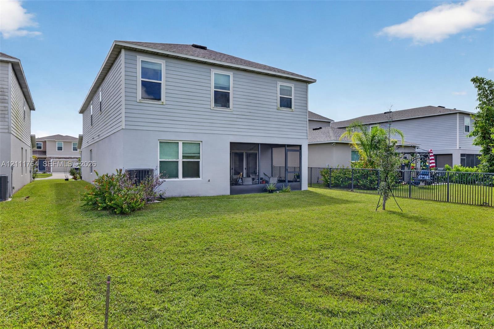 Two-story residence featuring light gray siding, a stucco lower exterior, a screened-in rear lanai, and a fenced backyard