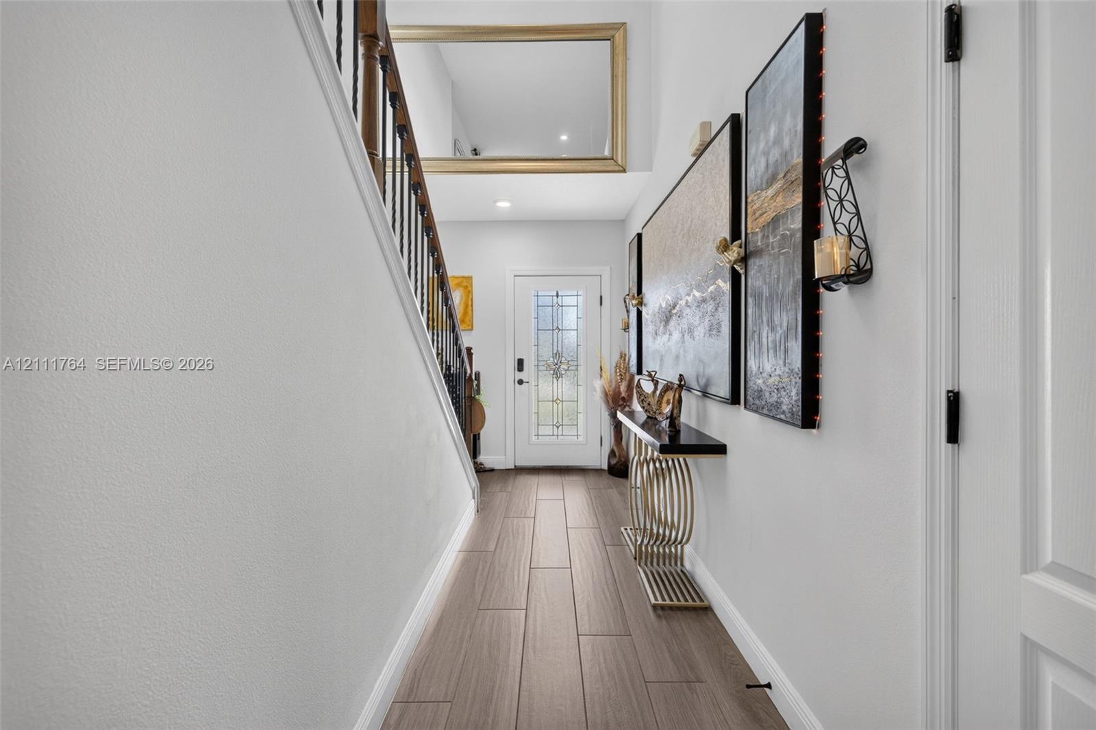 Entryway featuring wood-finish flooring, a decorative glass-panel front door, and a staircase with dark-toned balusters
