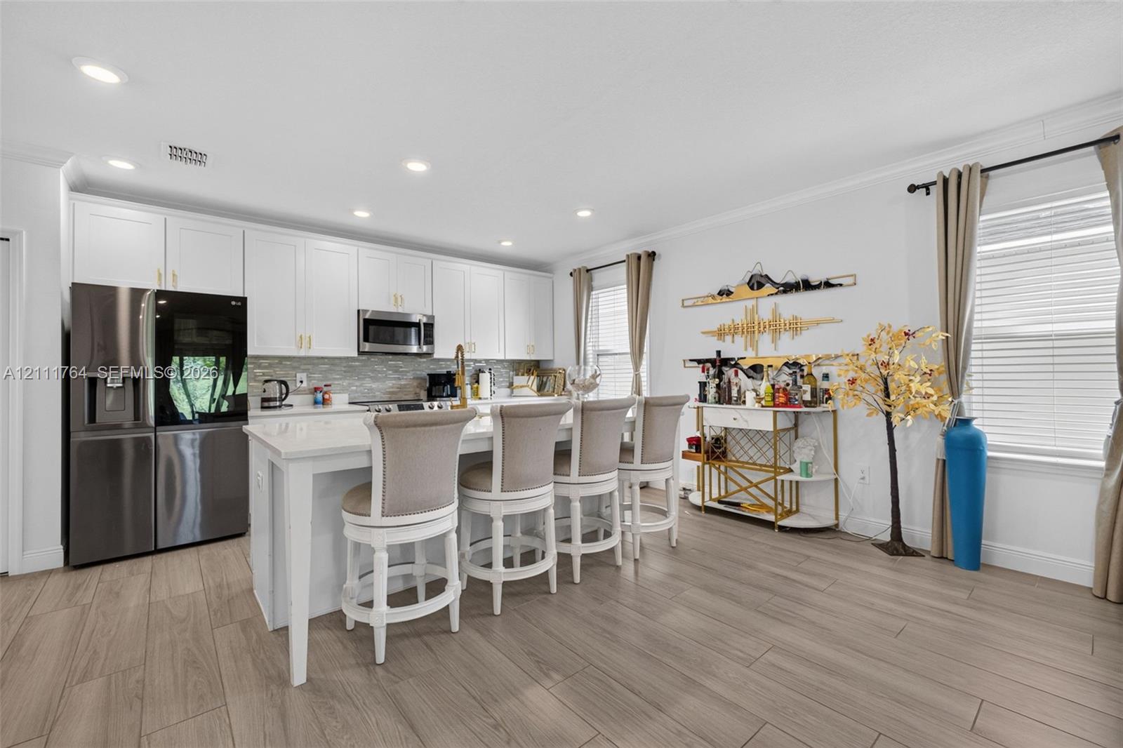 Kitchen featuring white shaker-style cabinetry, an expansive center island with stone countertop, stainless steel appliances, decorative stone-tiled backsplash, and wood-finish flooring