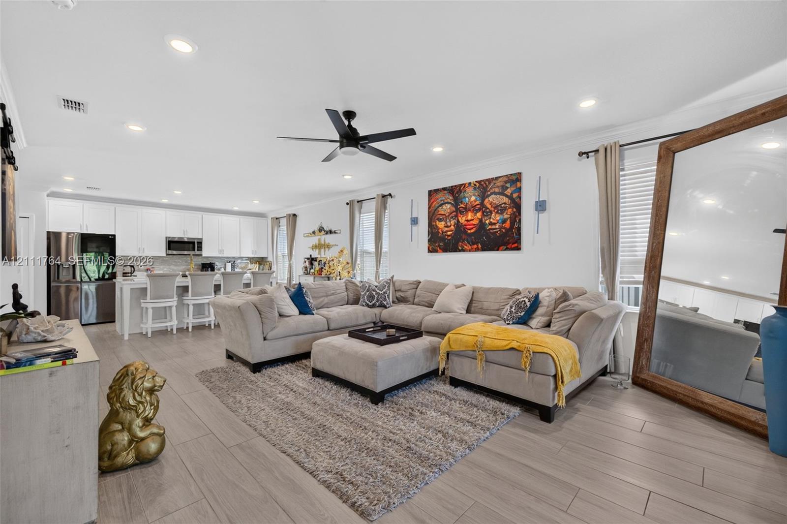 Open-concept interior featuring wood-finish flooring, recessed lighting, a modern ceiling fan, and white cabinetry with stainless steel appliances