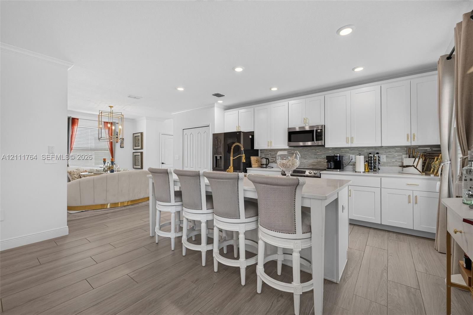 Kitchen featuring white shaker-style cabinetry, a central island with a quartz countertop, recessed lighting, wood-finish flooring, and a stone tile backsplash Kitchen featuring white shaker-style cabinetry, a central island with a quartz countertop, recessed lighting, wood-finish flooring, and a stone tile backsplash