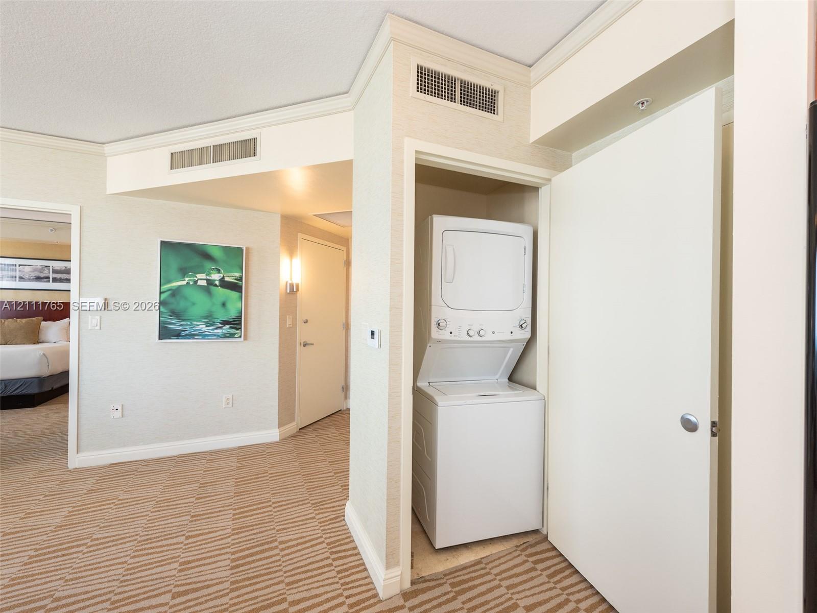 Built-in laundry closet with a stackable washer and dryer, textured wall treatments, and interior door hardware