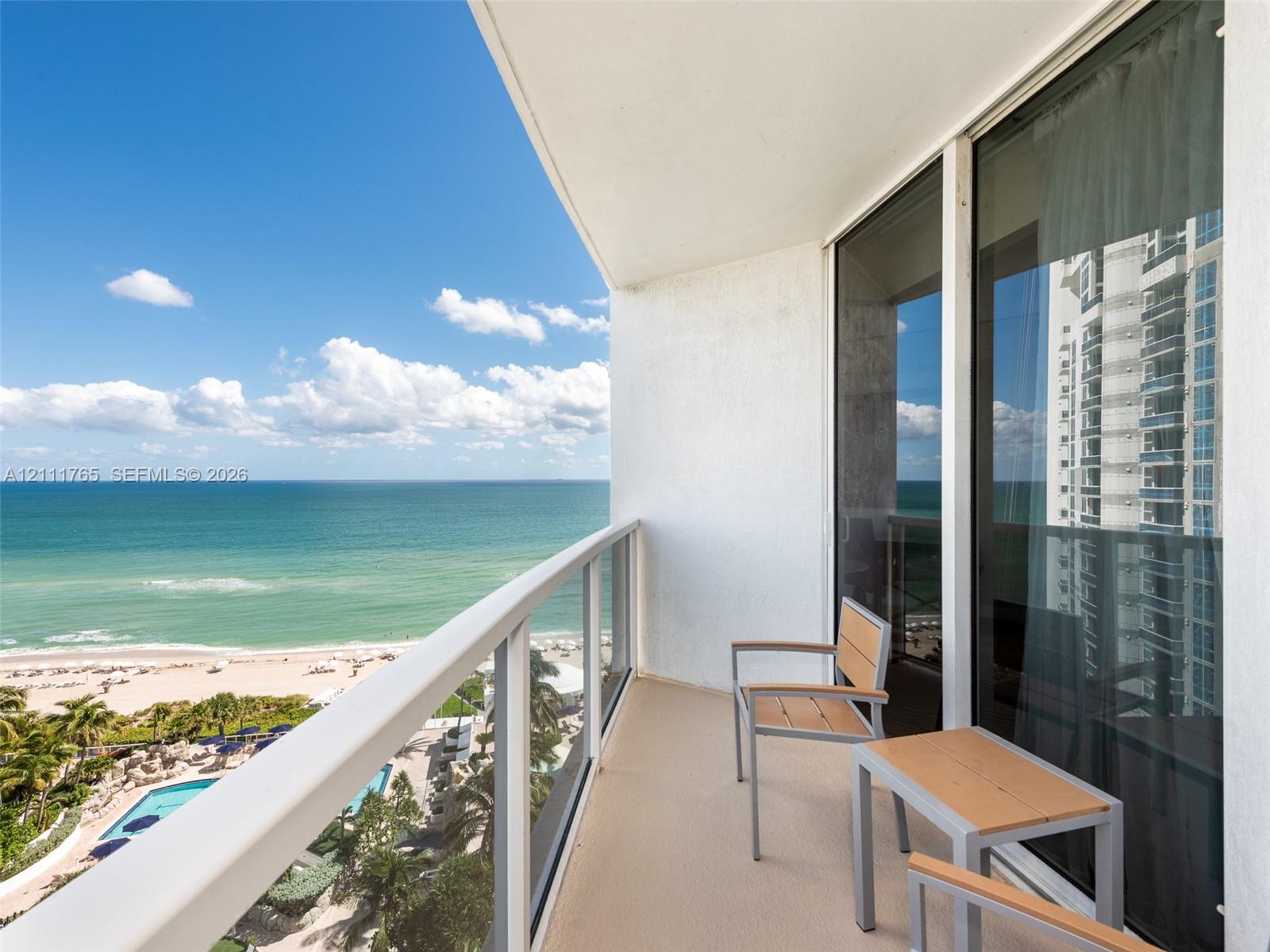 Private balcony featuring a glass-panel railing, solid-surface flooring, and expansive ocean and coastal scenery