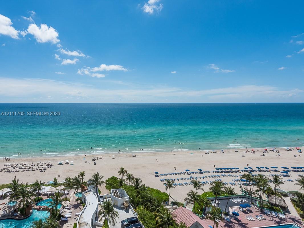 Oceanfront perspective featuring a sandy beach, turquoise water, mature palm trees, and an outdoor swimming pool