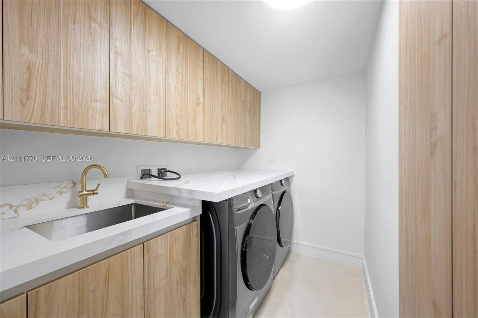 Utility space featuring custom wood-finish cabinetry, quartz countertops, stainless steel drop-in sink, and a brass-tone faucet