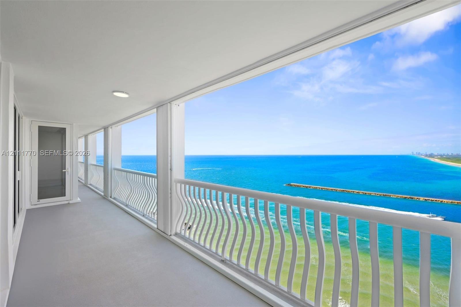 Covered balcony featuring a serpentine white railing, solid surface flooring, flush-mount lighting, and expansive ocean exposure