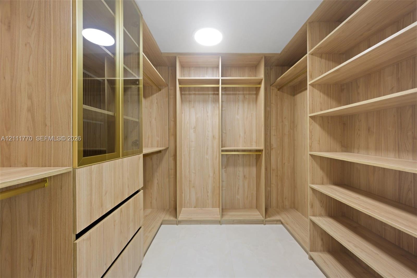 Custom wood-finish cabinetry featuring extensive open shelving, integrated hanging rods with metallic hardware, drawer storage, and a floor-to-ceiling glass-paneled cabinet