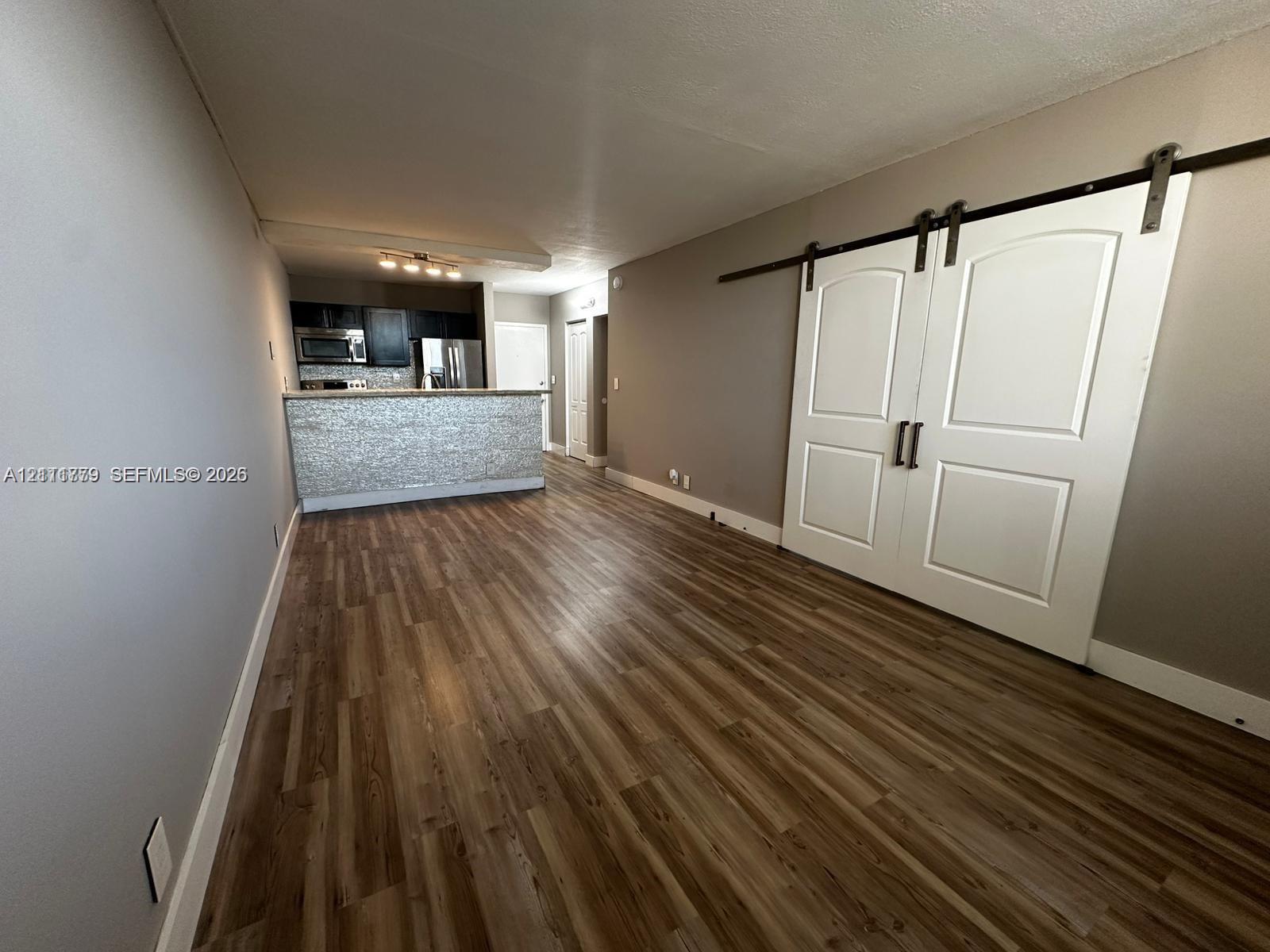 Wood-finish flooring throughout featuring double white barn doors with matte black hardware, stone-tiled breakfast bar, and stainless steel kitchen appliances