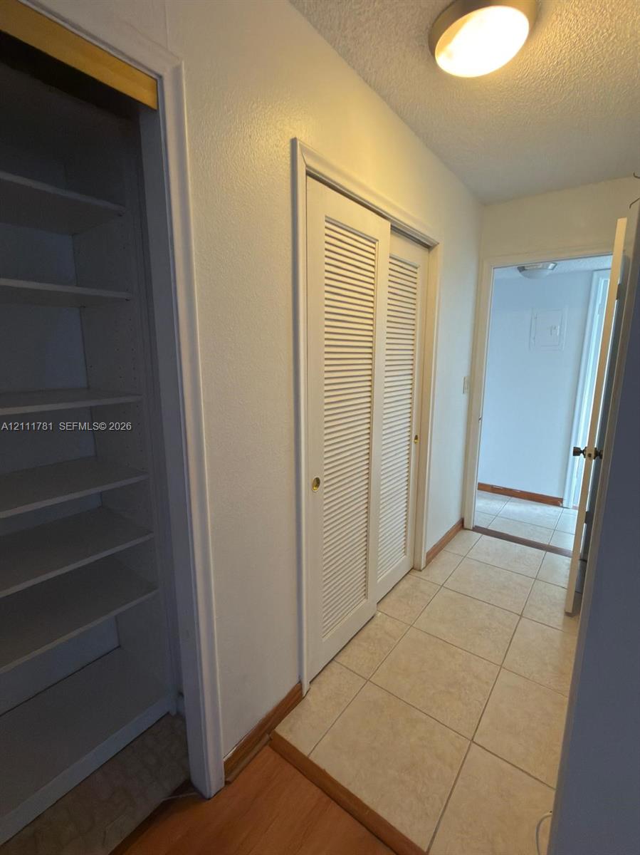 Built-in shelving units, dual louvered closet doors, and ceramic tile flooring