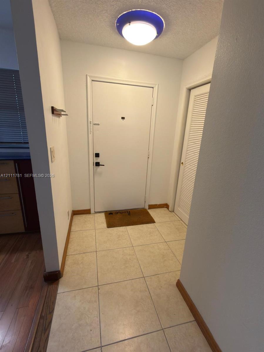 Entryway featuring large-format neutral floor tile, a solid door with matte black hardware, and a louvered closet door