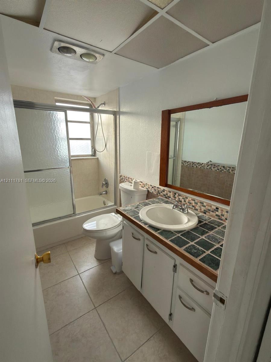 Bathroom featuring a vanity with a tiled countertop, drop-in sink, framed mirror, and a tub-shower combination with a sliding glass enclosure
