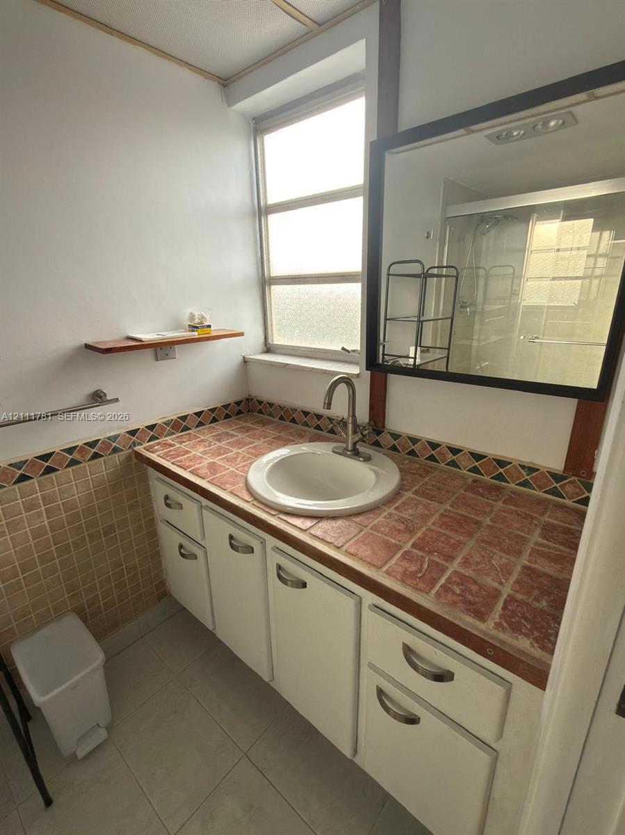 Vanity featuring a tiled countertop with decorative trim, an integrated circular sink, polished metal faucet, and white cabinetry