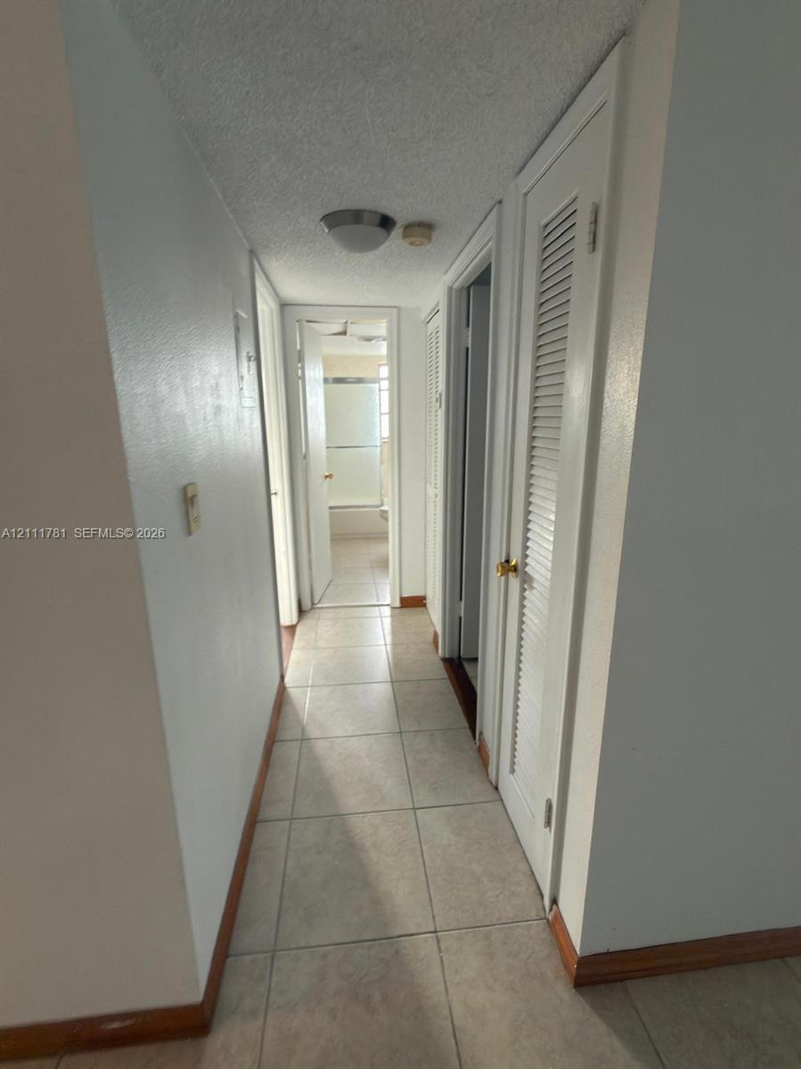 Hallway featuring ceramic tile flooring, neutral wall paint, and closet doors with louvered panels
