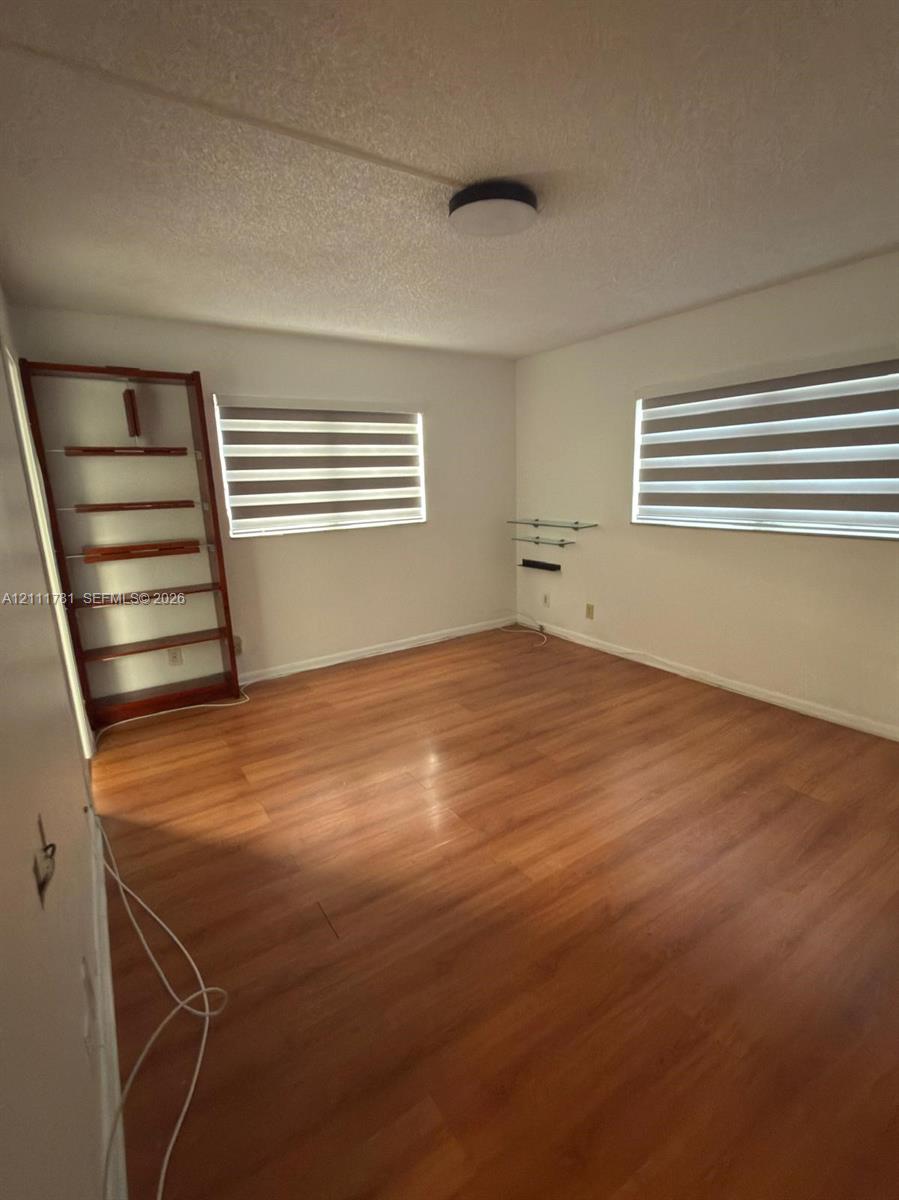 Room featuring wood-finish flooring, dual windows with fitted light-filtering shades, a built-in wooden shelving unit, and a central flush-mount ceiling fixture