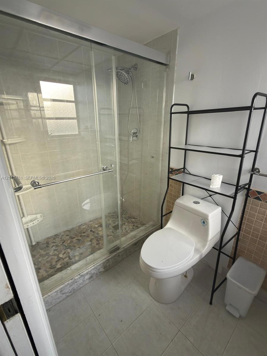 Walk-in shower featuring a sliding glass enclosure, pebble-stone flooring, and a wall-mounted showerhead, complemented by a dual-flush toilet and neutral tile wall accents