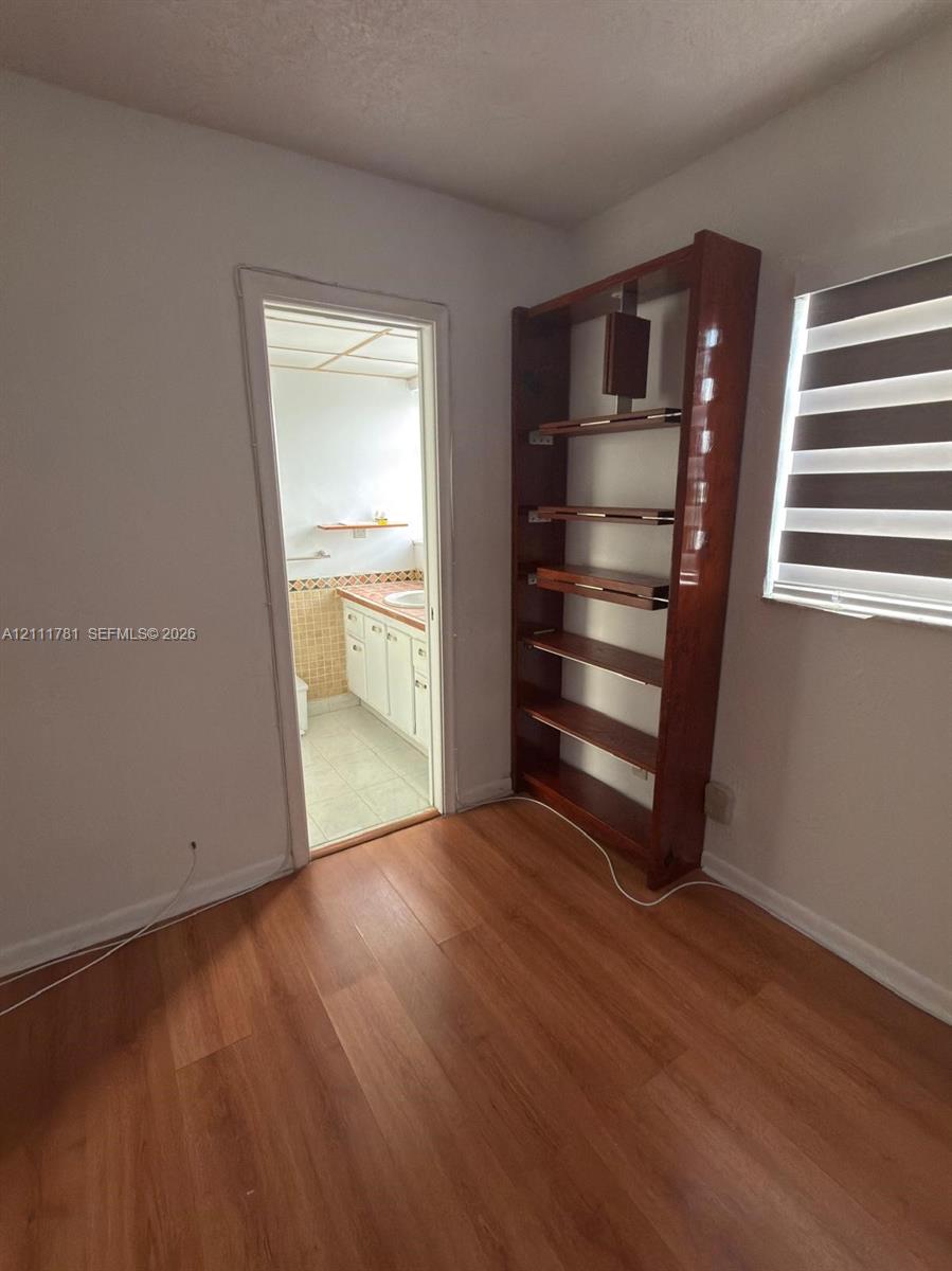 Wood-finish flooring, built-in wooden shelving unit, and a window with a dual-layer roller shade