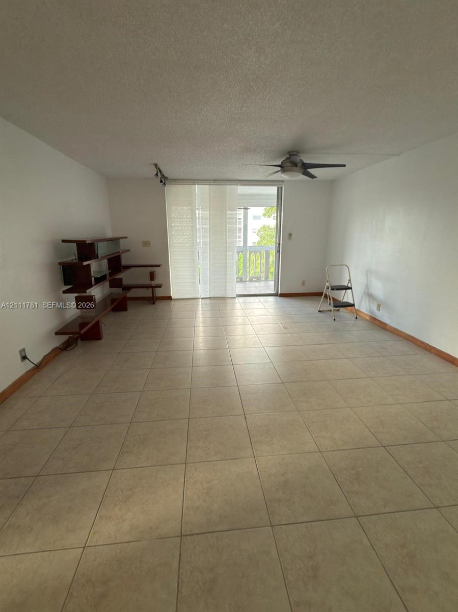 Neutral-toned ceramic tile flooring, ceiling-mounted fan, and glass sliding doors leading to an exterior balcony