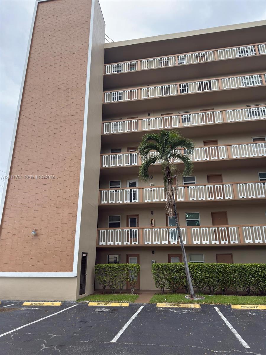 Multi-story building exterior featuring textured masonry siding, stacked private balconies with geometric railings, and reserved surface parking