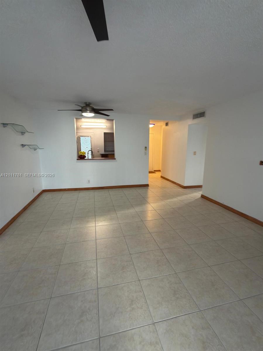 Interior space featuring neutral tile flooring, ceiling-mounted fan, and wall-mounted glass display shelving