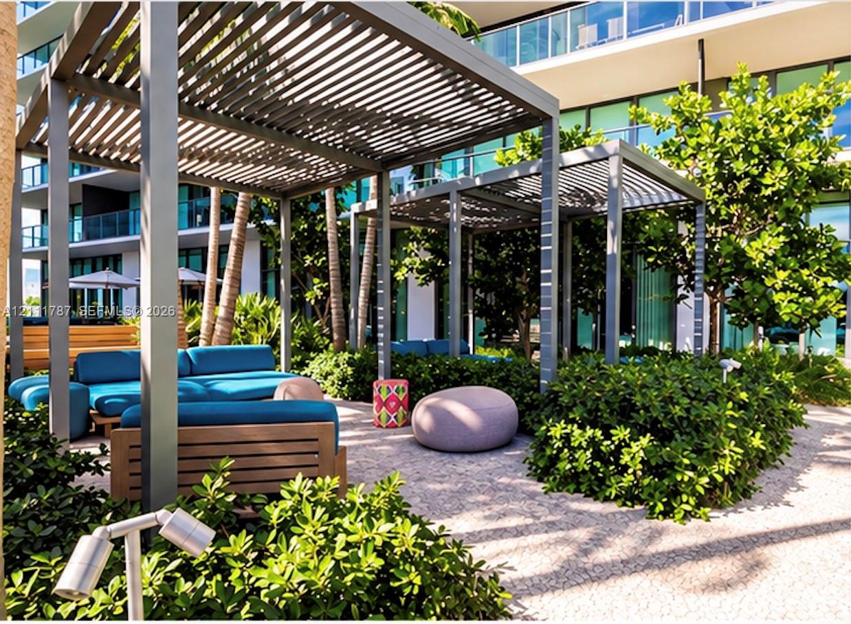 Outdoor lounge area featuring dual metal pergolas, stone paver flooring, integrated landscaping, and privacy shrubbery