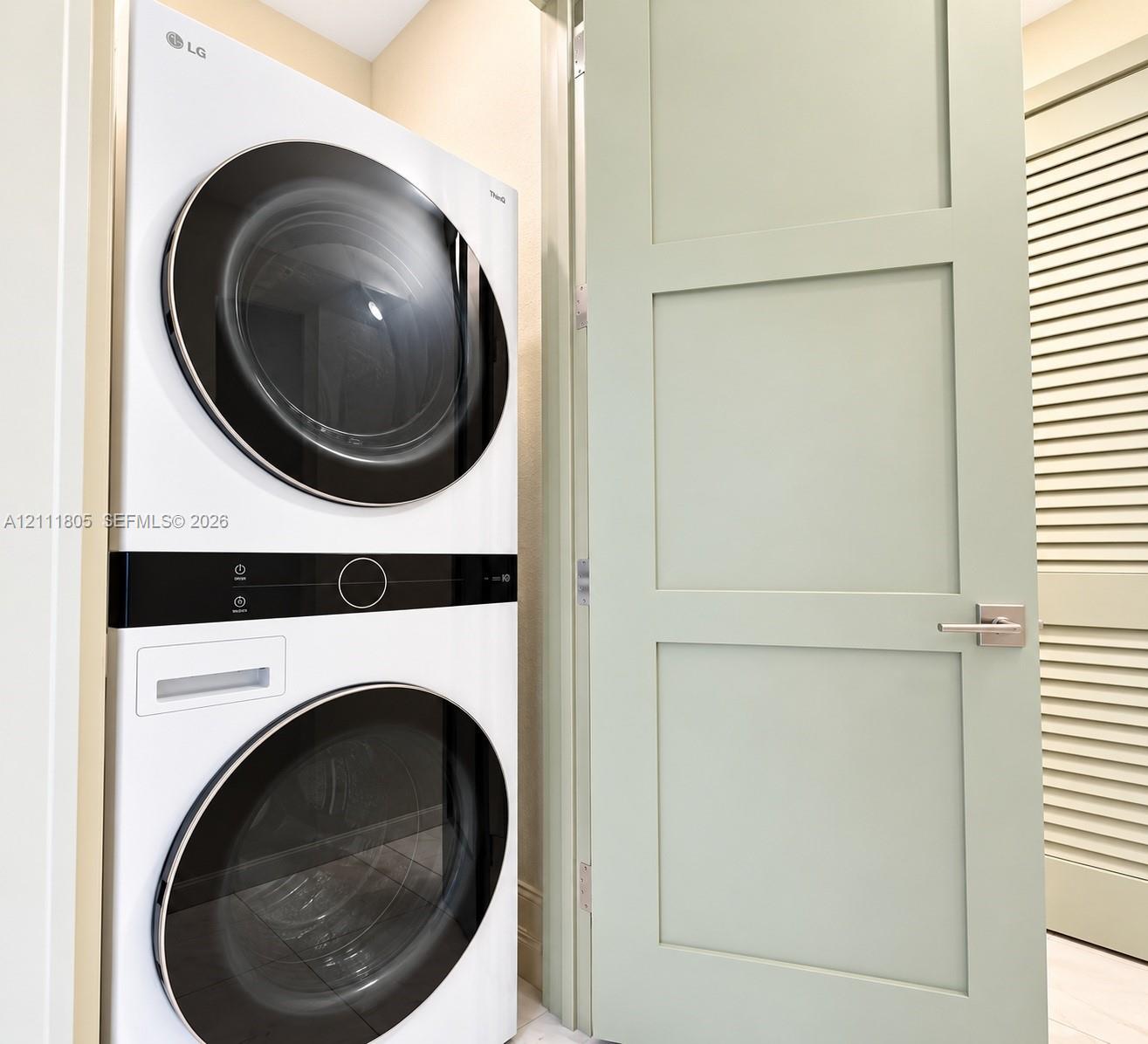 Stacked white LG washer and dryer unit with circular glass doors and central digital interface, pale green shaker-style door with satin nickel lever hardware, and louvered panel door