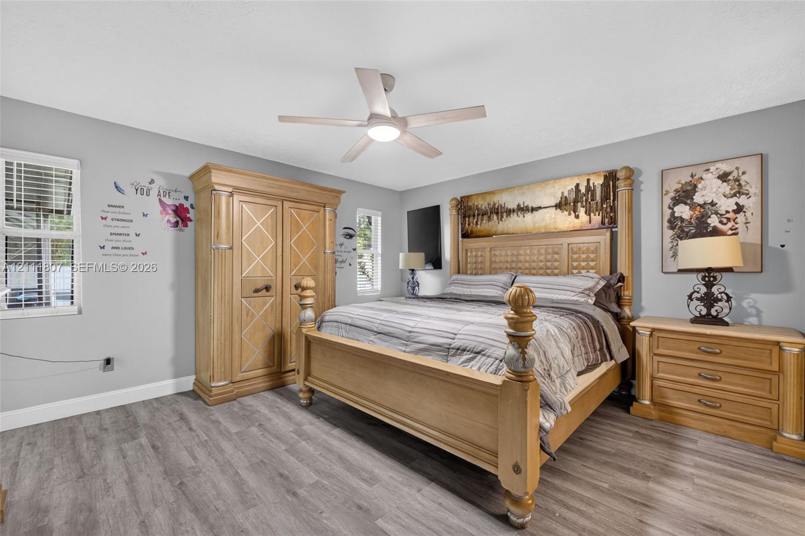 Room featuring wood-finish flooring, dual windows, and a ceiling fan with integrated lighting