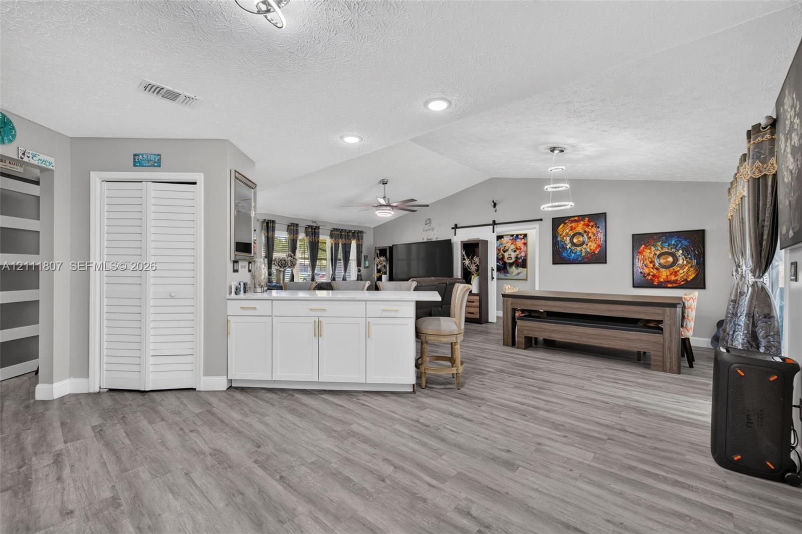 Vaulted ceilings, wood-finish flooring, white kitchen island with cabinetry, recessed lighting, and sliding barn door