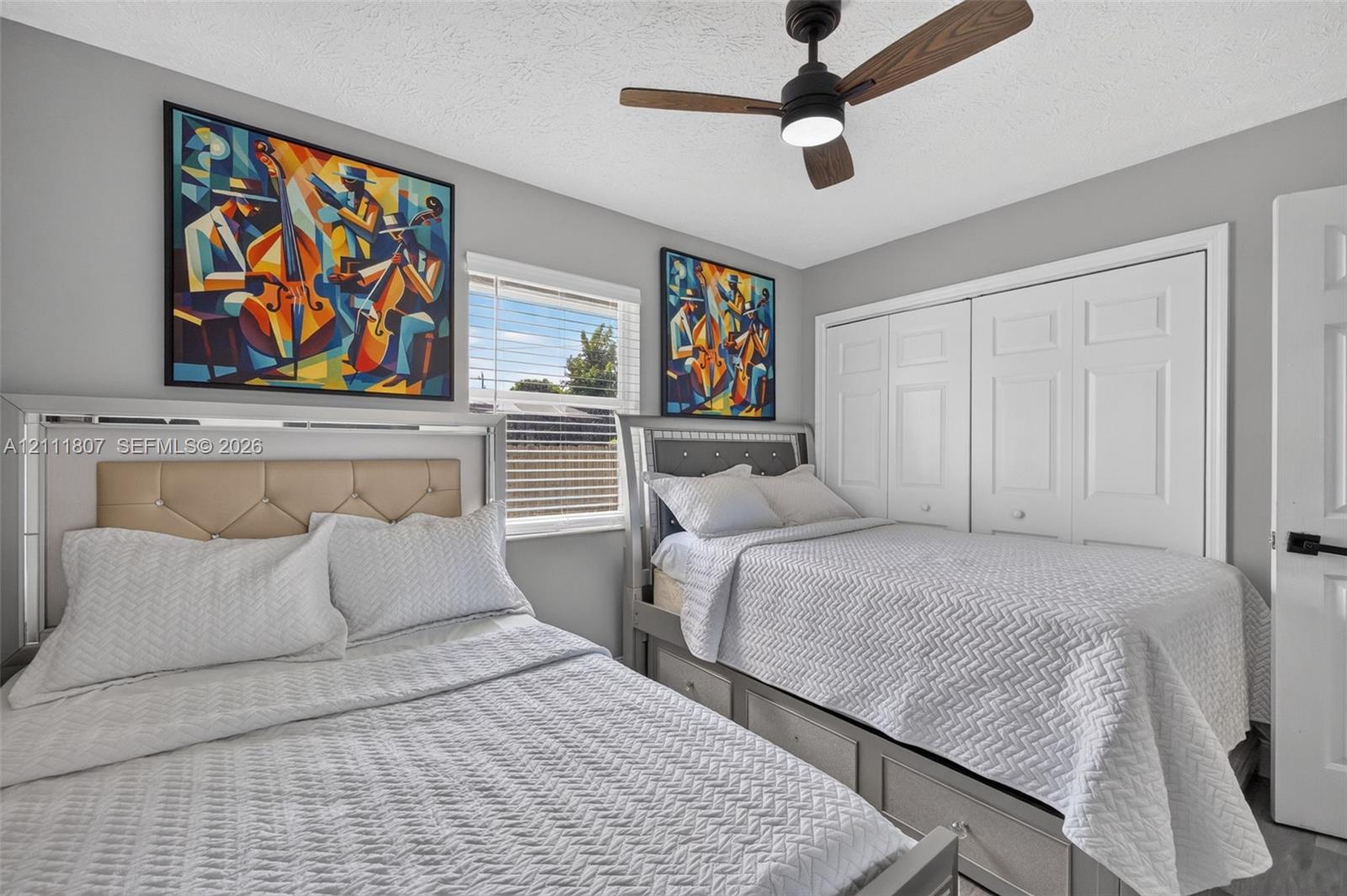 Neutral-toned bedroom featuring a matte black ceiling fan with integrated lighting, white dual-panel closet doors, horizontal blind window treatment, and gray interior walls