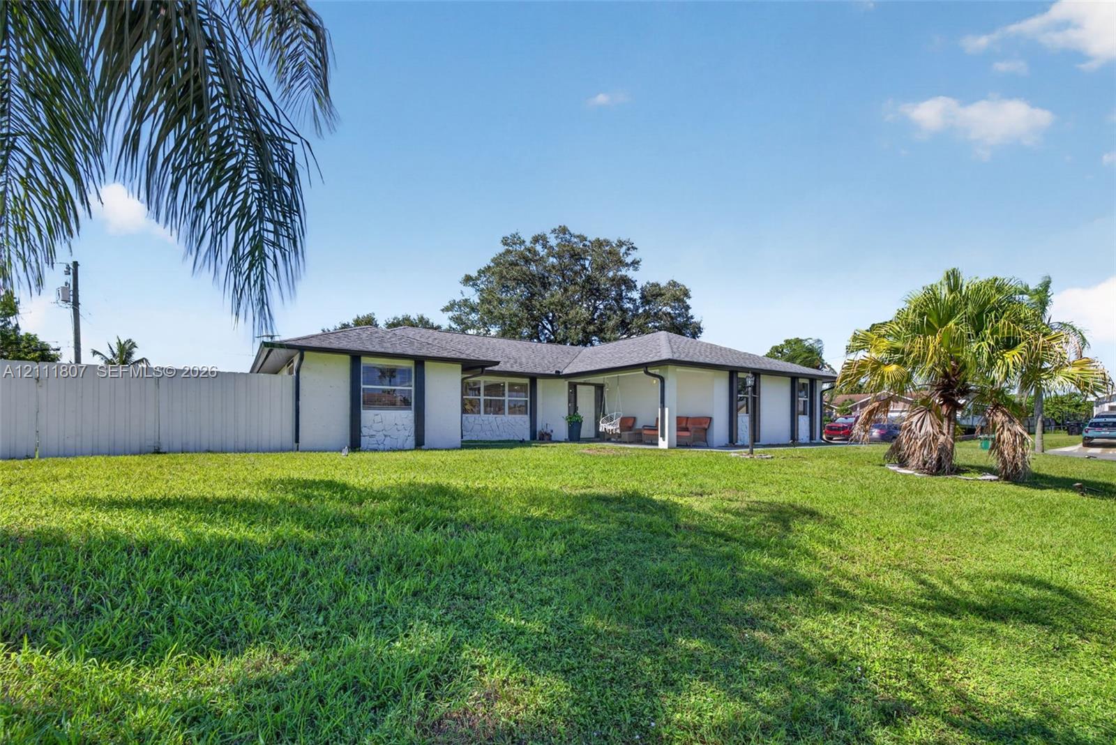 Single-story exterior featuring a hip roof, stucco facade, covered porch, and privacy fencing on a grass-covered lot Single-story exterior featuring a hip roof, stucco facade, covered porch, and privacy fencing on a grass-covered lot