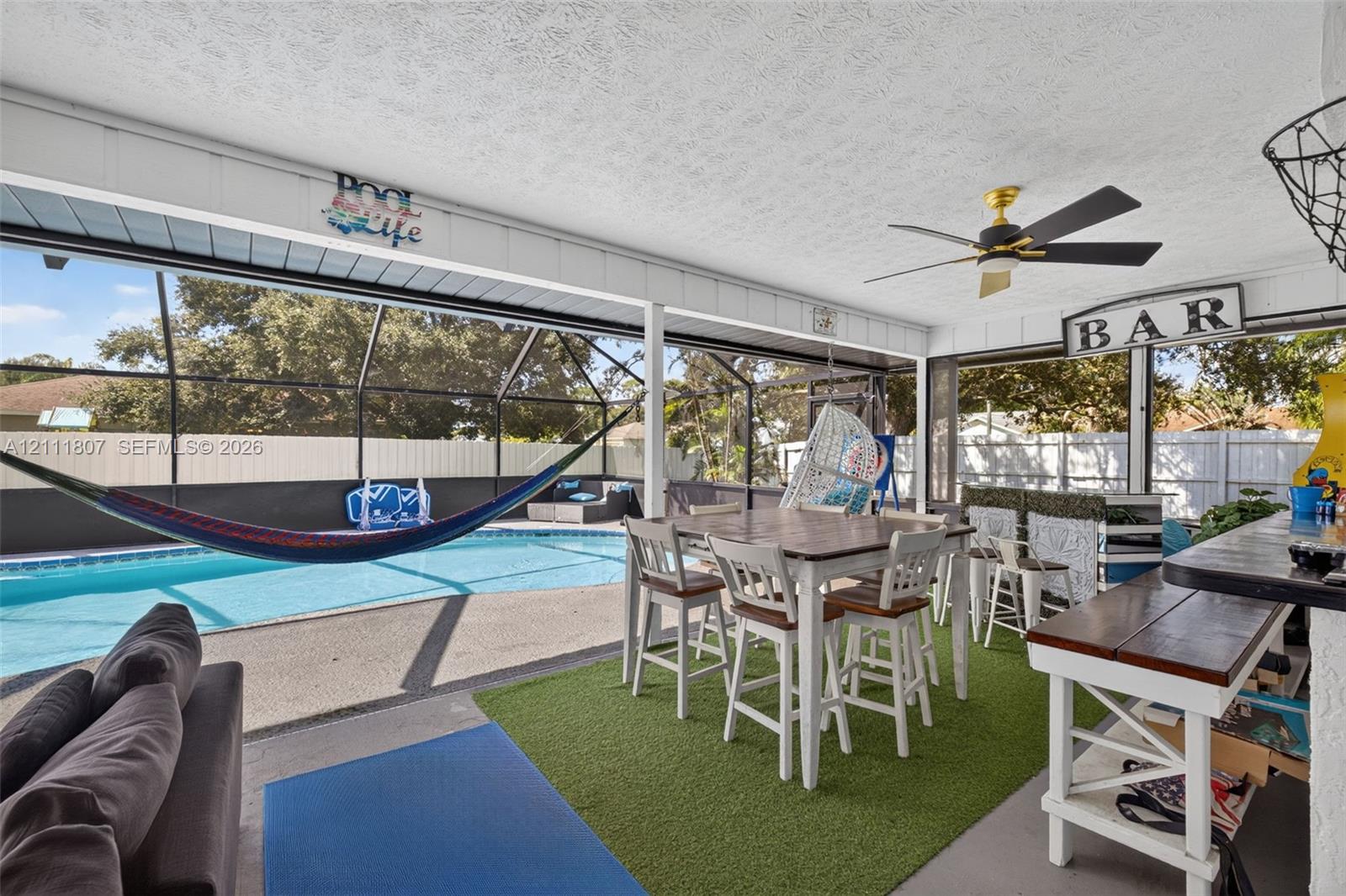 Screened-in lanai featuring a concrete patio, a ceiling fan, and a built-in bar, overlooking an in-ground swimming pool