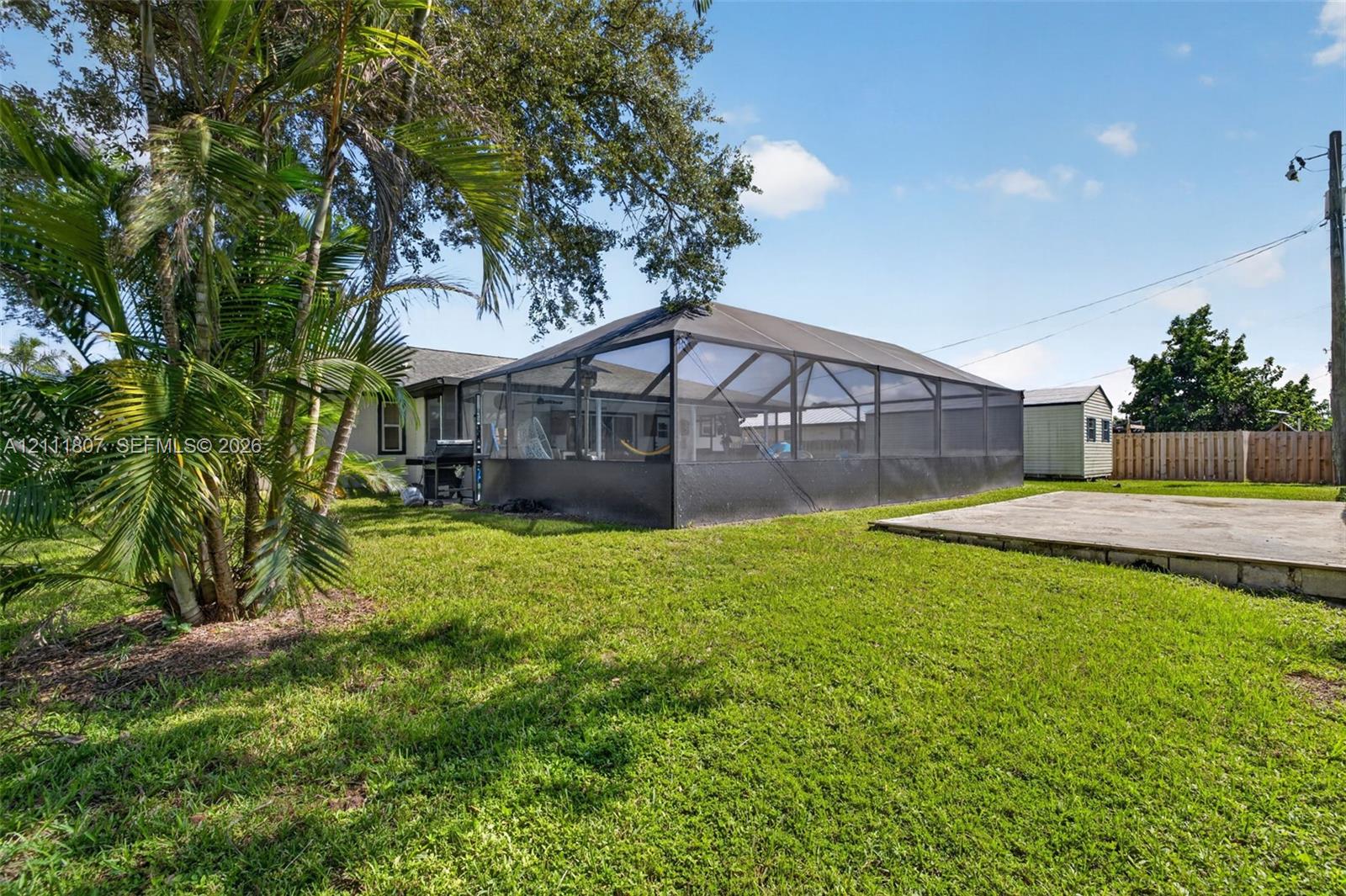 Backyard featuring a screened-in lanai, concrete patio, perimeter wood fencing, and mature landscaping