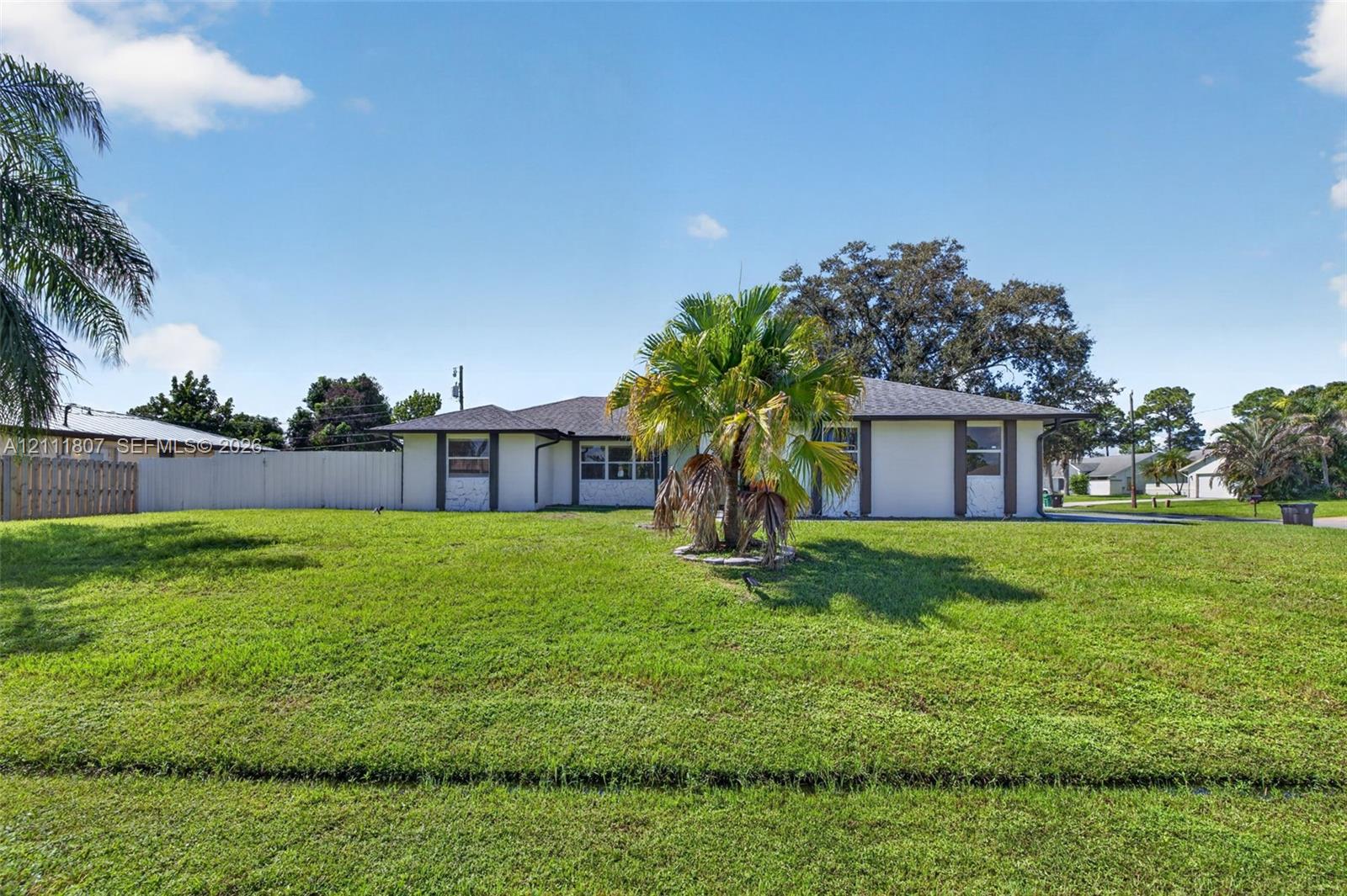 Single-story exterior featuring a light-toned stucco facade, shingled hip roof, expansive grassy lawn, and privacy fencing Single-story exterior featuring a light-toned stucco facade, shingled hip roof, expansive grassy lawn, and privacy fencing