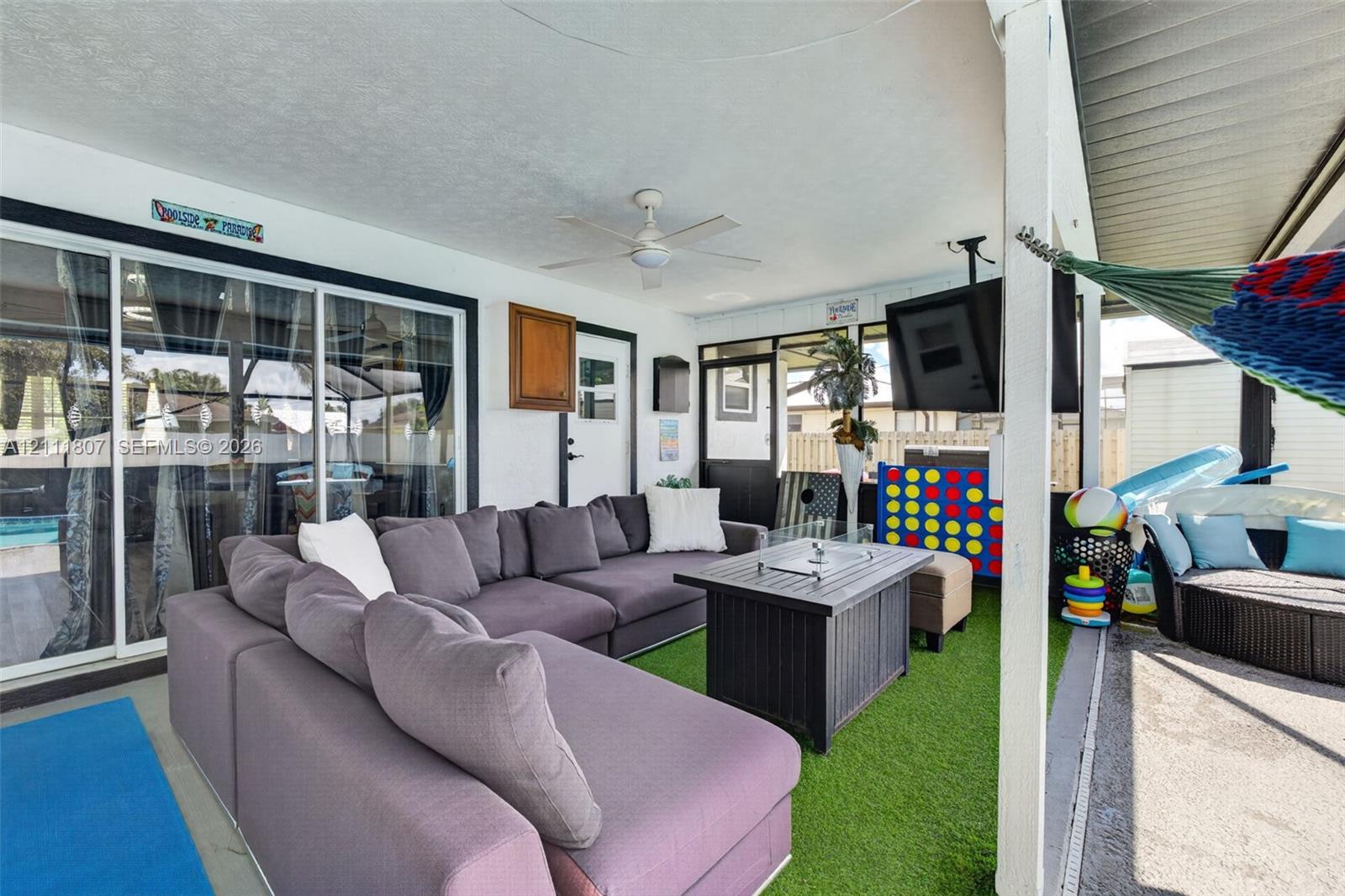 Covered patio featuring a ceiling fan, sliding glass doors, synthetic grass flooring, and screen enclosure