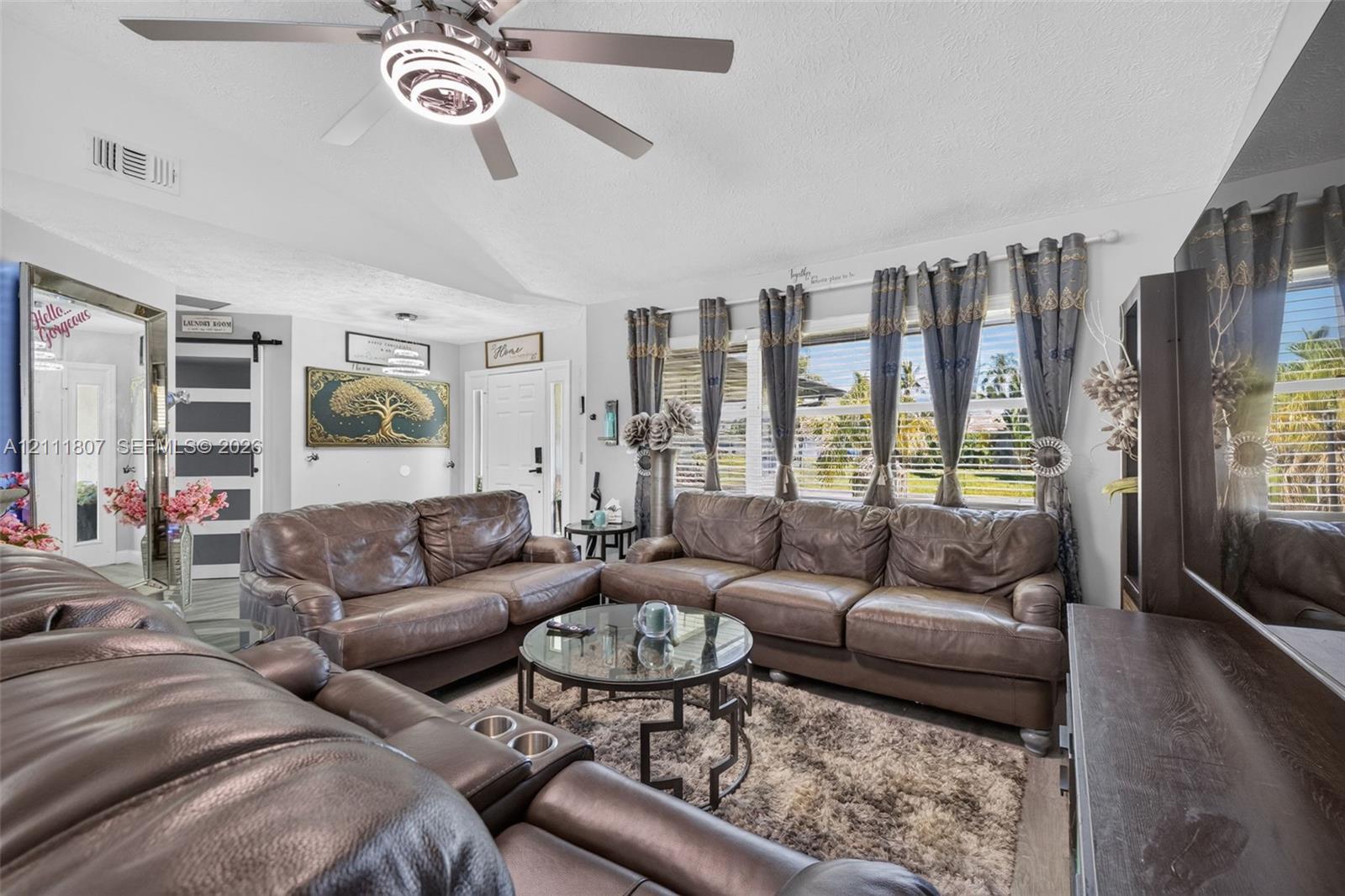 Vaulted ceilings featuring a central multi-light ceiling fan, large windows with horizontal blinds, and a sliding barn-style door Vaulted ceilings featuring a central multi-light ceiling fan, large windows with horizontal blinds, and a sliding barn-style door