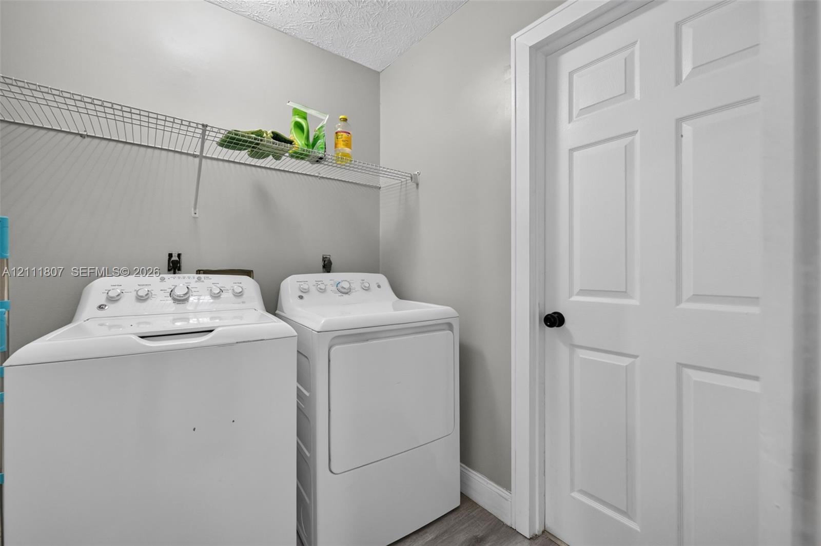 Dedicated laundry area featuring a white six-panel door, wall-mounted wire shelving, and neutral-toned wall paint