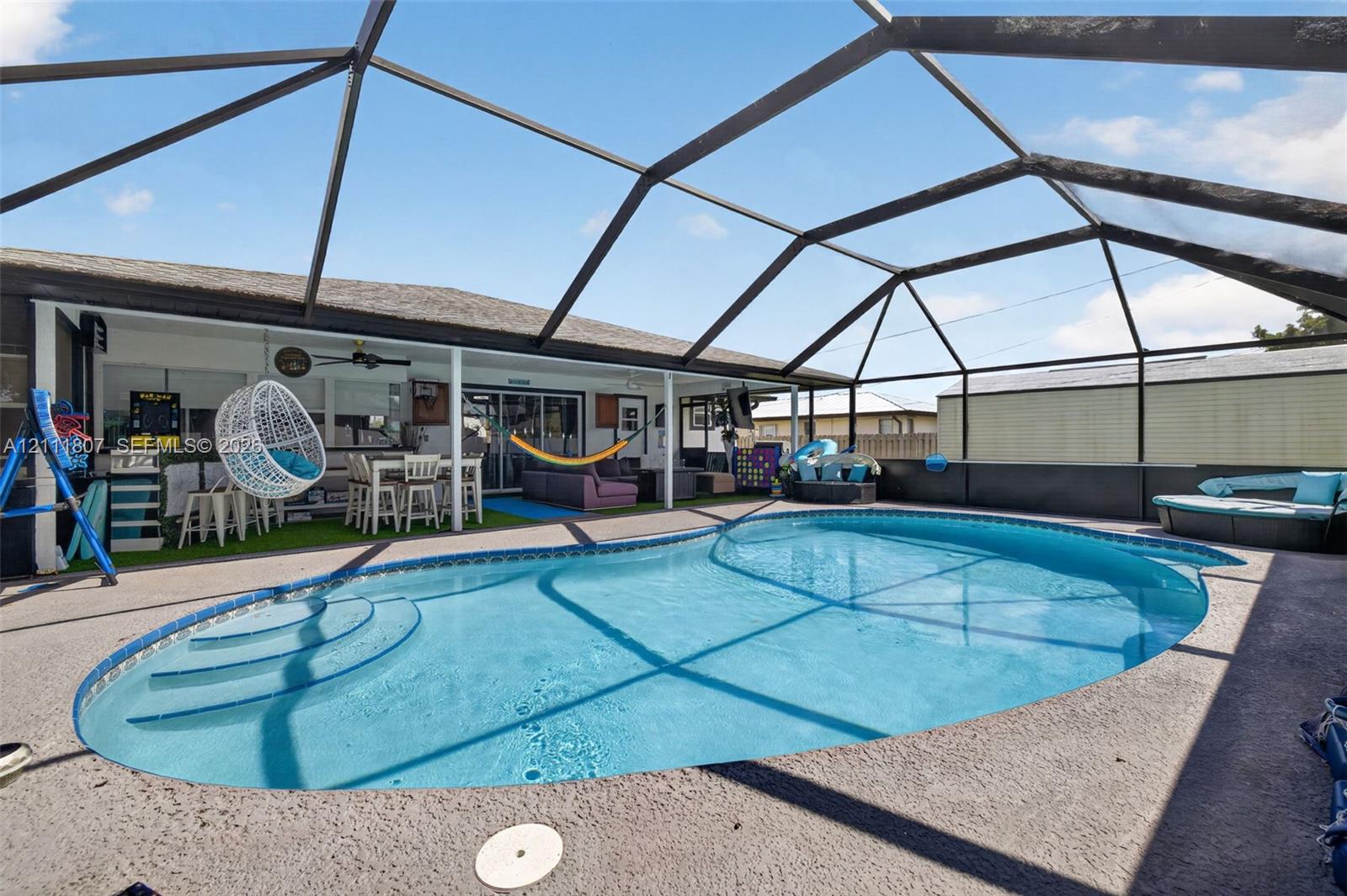 Screened-in patio area featuring a freeform swimming pool, integrated entry steps, and concrete decking