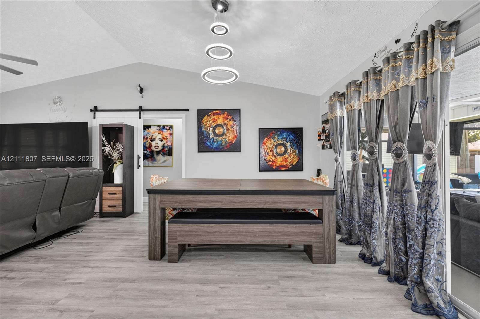 Vaulted ceilings, wood-finish flooring, sliding barn door with black iron hardware, and multi-tier circular pendant lighting