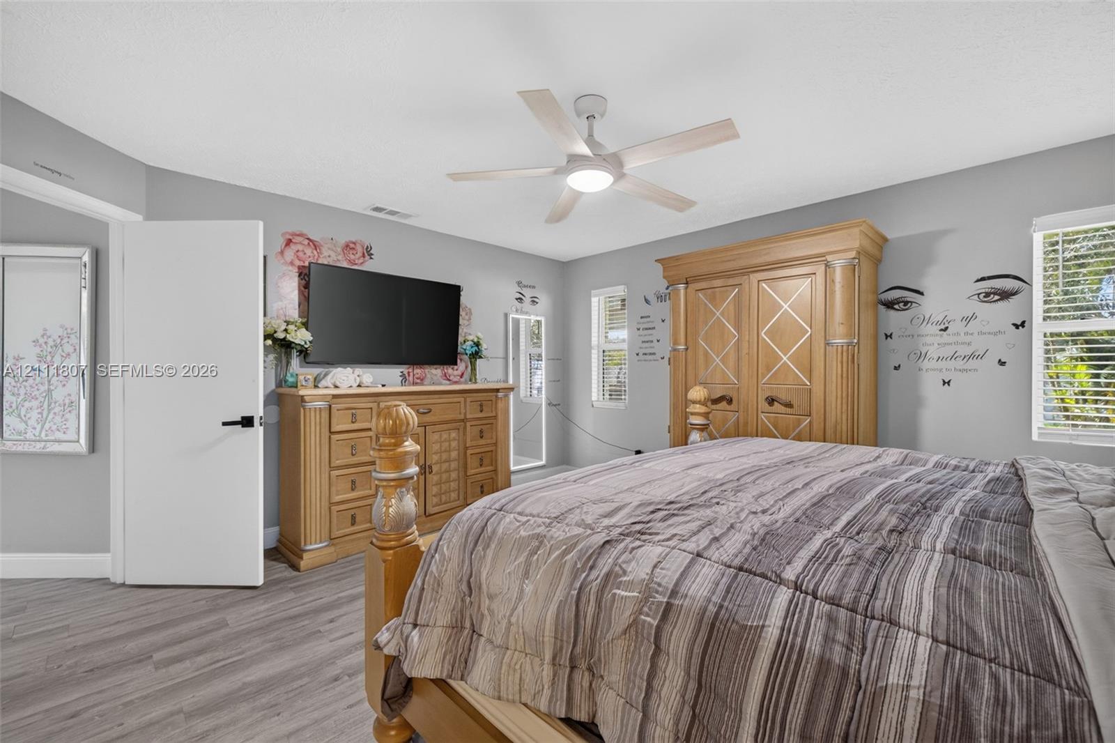 Wood-finish flooring, central ceiling fan with integrated lighting, and white interior doors with matte black hardware