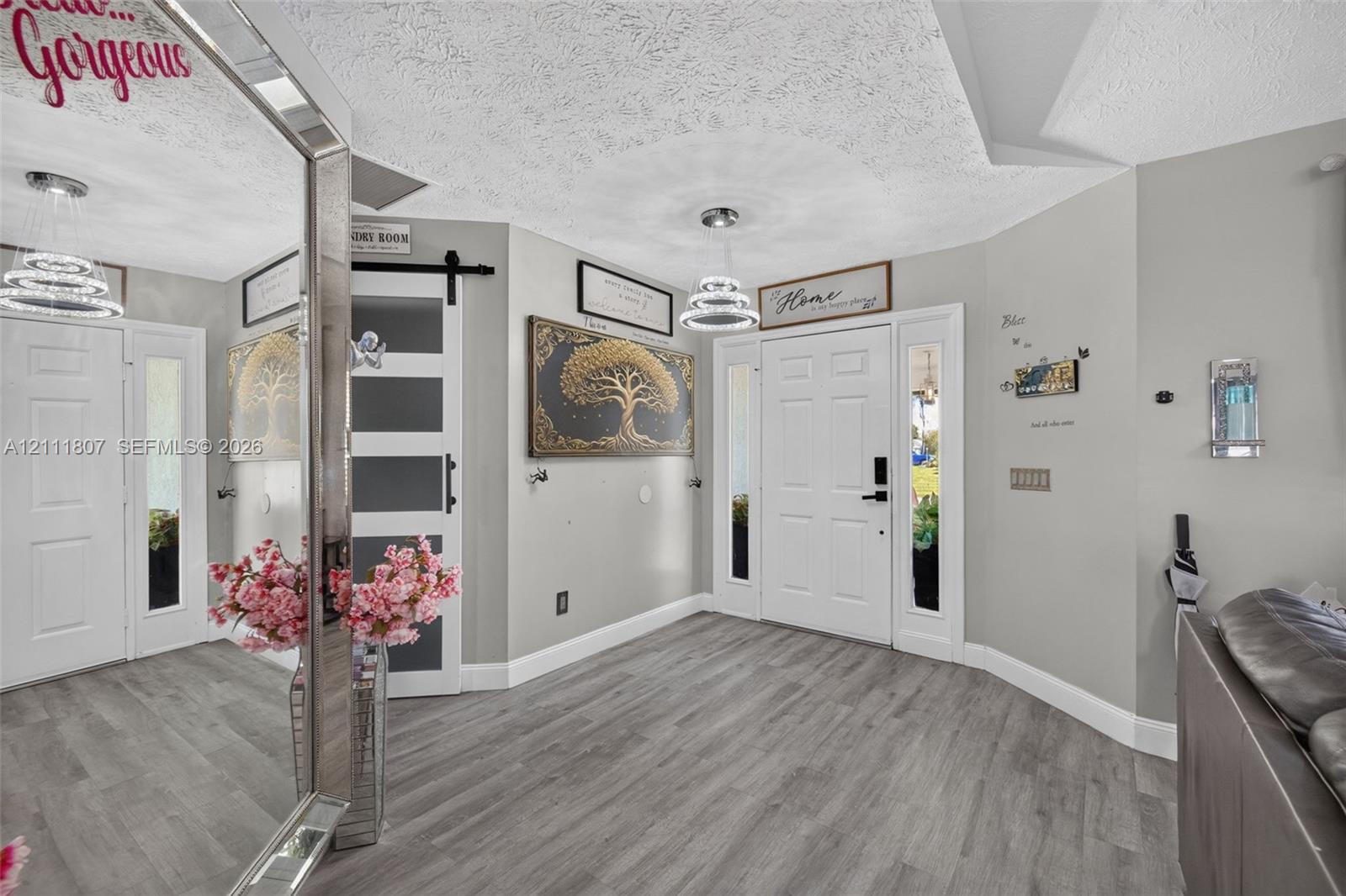 Entryway featuring wood-finish flooring, a sliding barn door with glass panes, white six-panel doors with side lites, and multi-tiered modern pendant lighting Entryway featuring wood-finish flooring, a sliding barn door with glass panes, white six-panel doors with side lites, and multi-tiered modern pendant lighting