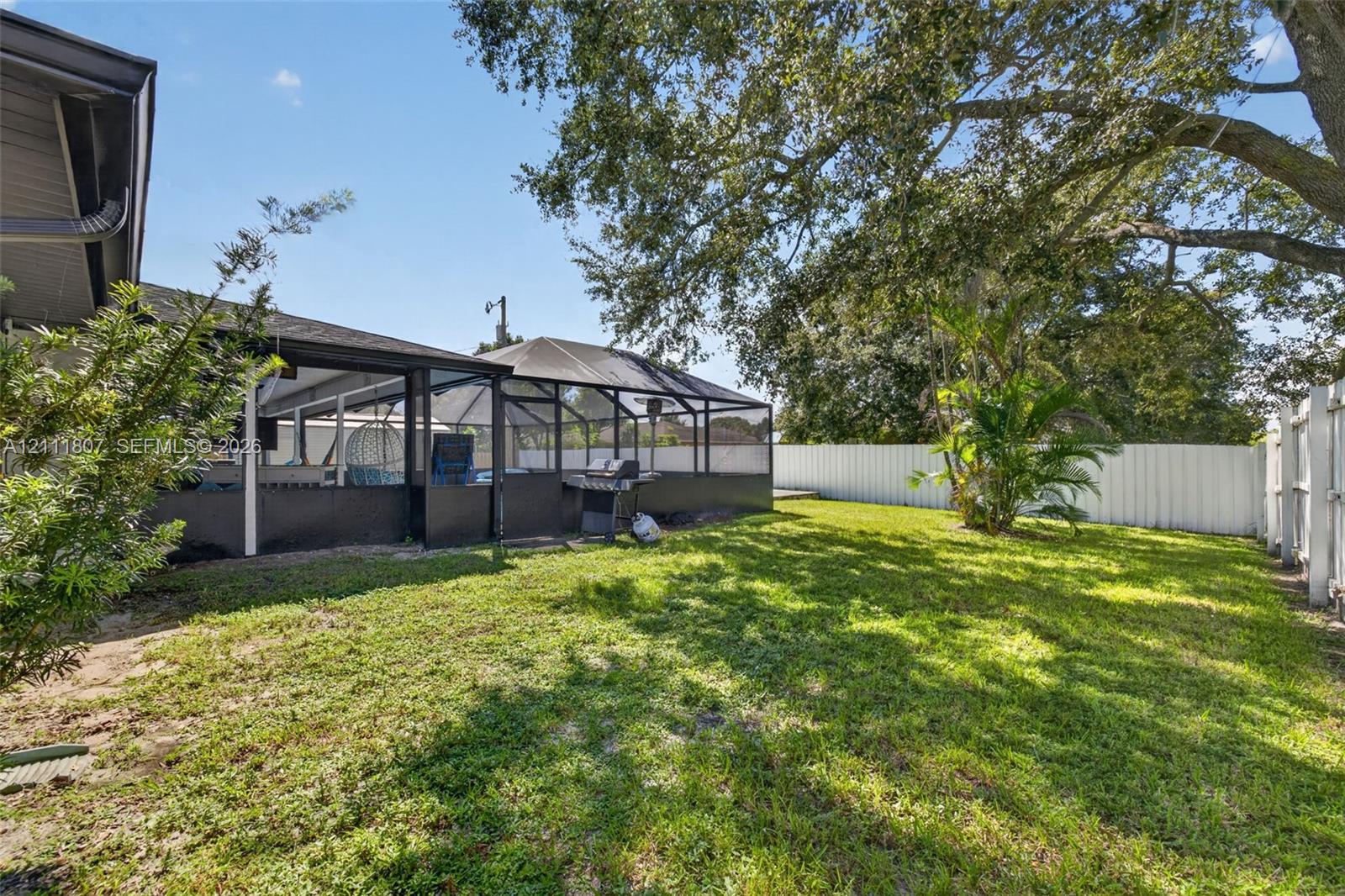 Backyard featuring a screened-in lanai, privacy fencing, mature trees, and a grass lawn