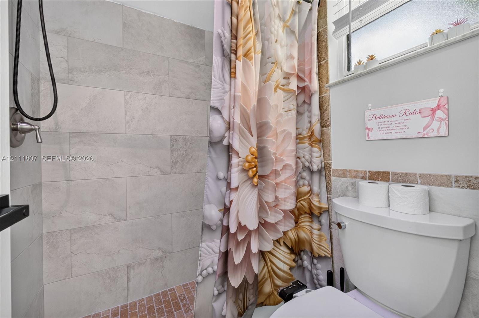 Walk-in shower featuring large-format neutral tile walls, a mosaic tile floor, and a handheld shower fixture