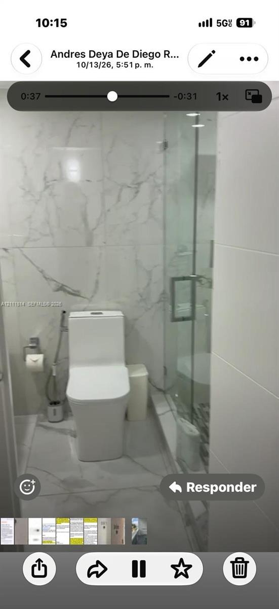 Bathroom featuring large-format veined porcelain tile wall and floor surfaces, glass-enclosed shower, and a minimalist low-profile dual-flush toilet