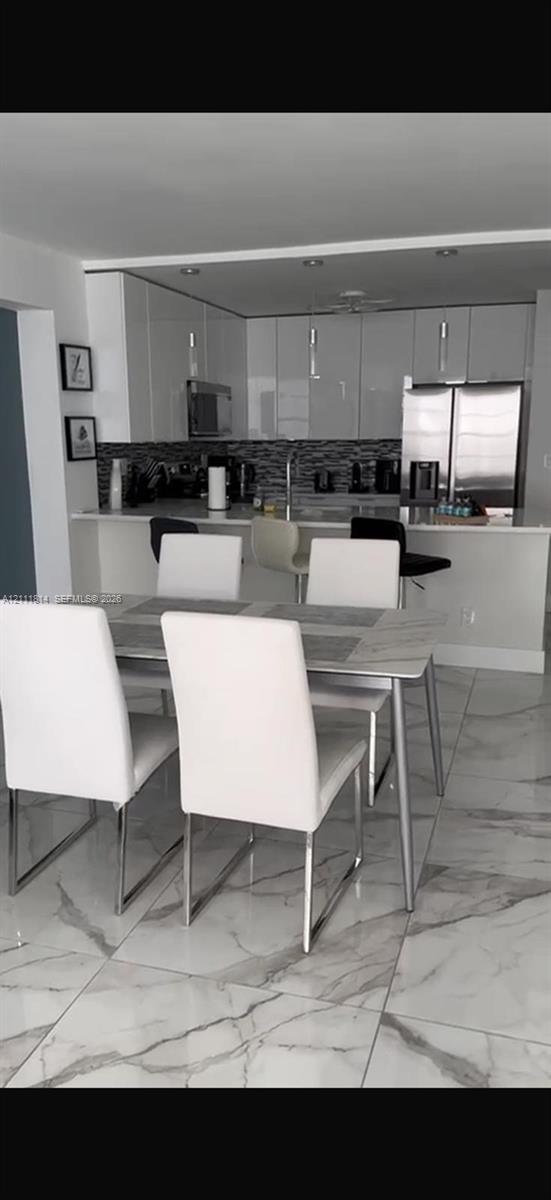 Kitchen featuring flat-panel high-gloss cabinetry, stone-finish countertops, stainless steel appliances, mosaic tile backsplash, and large-format tile flooring