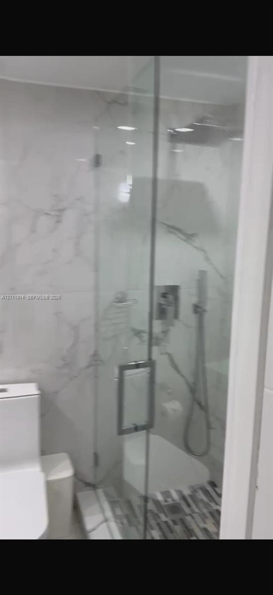 Walk-in glass-enclosed shower featuring large-format stone-patterned wall tile, rain-style shower head, handheld sprayer, and mosaic tile floor inlay