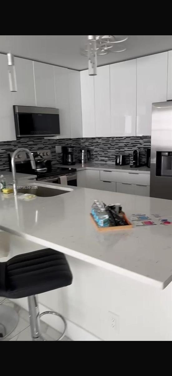 Kitchen featuring gloss-finish cabinetry, stone-surface countertops, stainless steel appliances, a multi-tone tile backsplash, and a built-in island