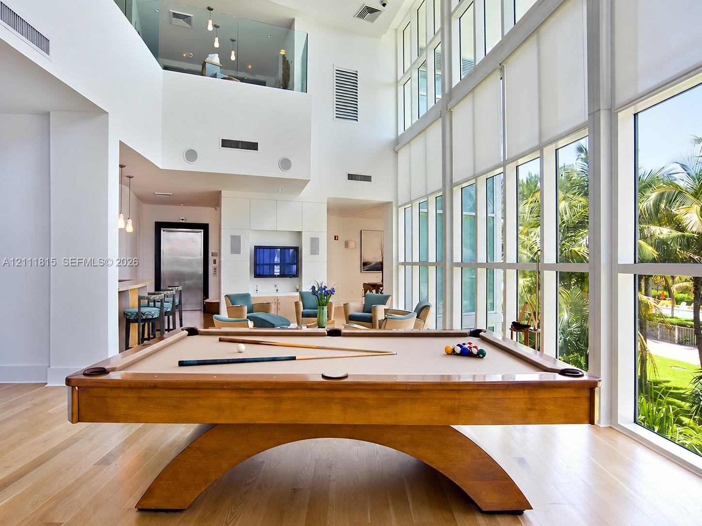 Double-height ceiling, floor-to-ceiling windows, wood-finish flooring, built-in wet bar, and glass-paneled mezzanine railing Double-height ceiling, floor-to-ceiling windows, wood-finish flooring, built-in wet bar, and glass-paneled mezzanine railing