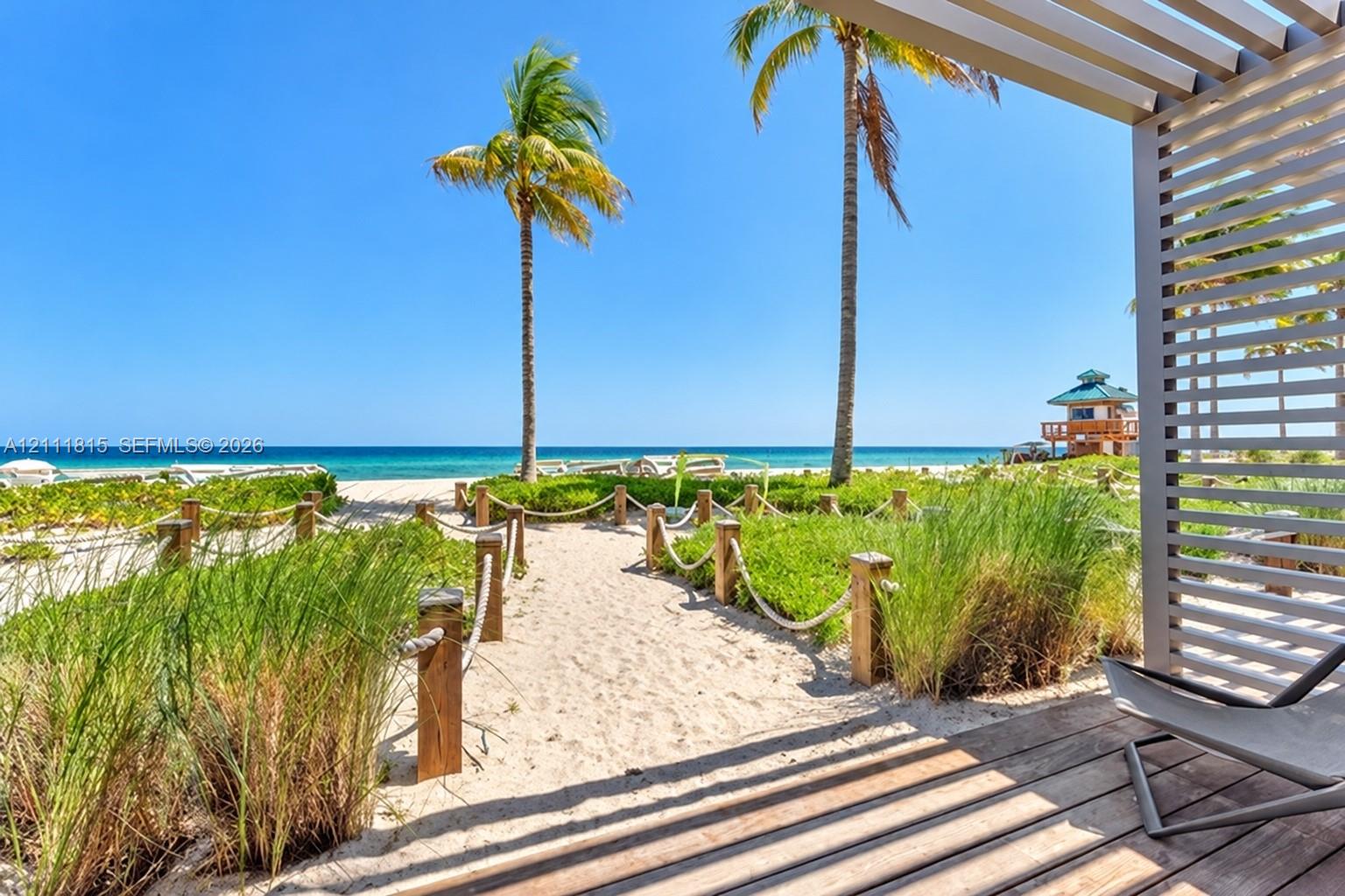 Covered wood deck with slatted privacy screen, sand path with rope perimeter, and coastal landscaping